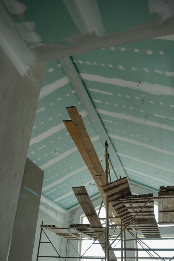 Scaffolding setup in an interior construction space with suspended ceiling boards and wooden planks.